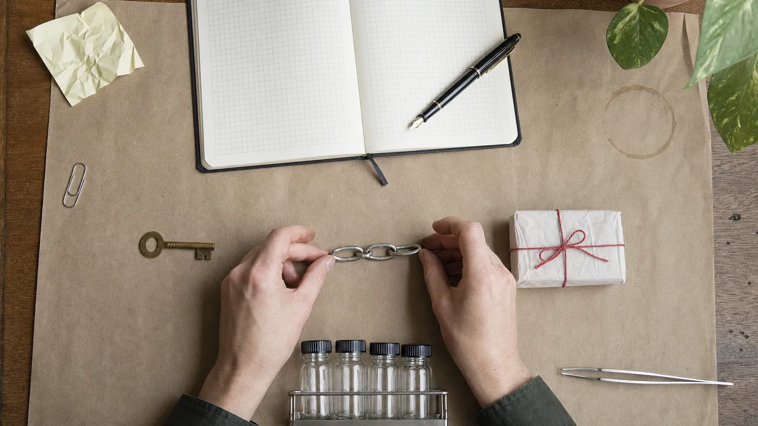 Overhead view of a key, a short chain and a small wrapped parcel in a line, with vials and a notebook.