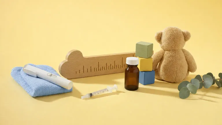 Studio still life of a growth ruler, injection pen, wooden blocks and a stuffed bear on yellow paper