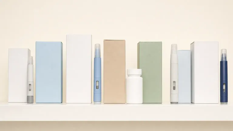A row of plain medicine boxes, injection pens and a pill bottle lined up on a shelf.
